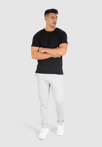 Musta puuvillainen t-paita yhdistettynä vaaleanharmaisiin collegehousuihin. Mallilla on valkoiset lenkkarit. Yksinkertainen muotoilu, jossa on lyhyet hihat ja pyöreä pääntie.