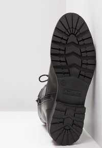 Botte en cuir noir avec bout rond, design à lacets, fermeture éclair latérale et semelle en caoutchouc texturée avec motif de bande de roulement. Taille 37 visible.