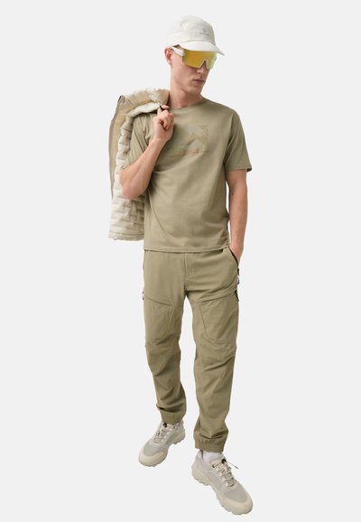 Khaki t-shirt med subtilt logo, matchende cargo-bukser med lommer, hvid pufferjakke draperet, sporty kasket, reflekterende solbriller, teksturerede sneakers.