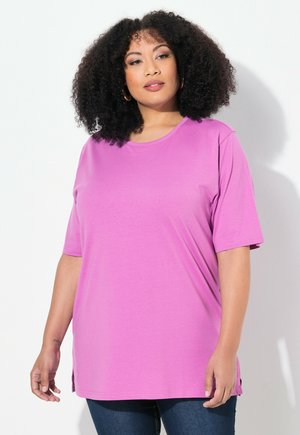 T-shirt rosa di taglio ampio in tessuto morbido, con colletto a giro, maniche corte e aperture laterali per facilitare i movimenti.