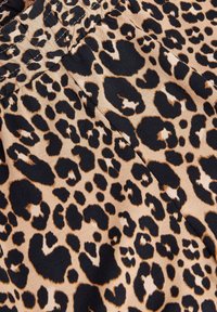 Leopardmønstret stof med en lys tan-bund og store sorte og brune pletter. Glat tekstur med et let strækbart materiale.