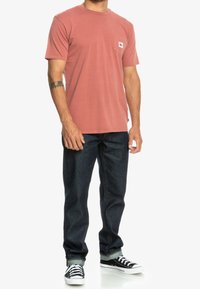 Pánské tričko s krátkým rukávem v korálově růžové barvě, s kapsou na prsou, spárované s tmavě modrými džínami a černobílými teniskami.