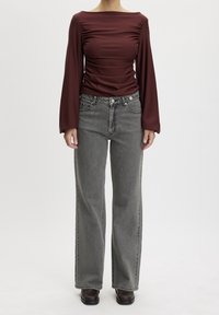 Maglietta a maniche lunghe bordeaux con dettagli arricciati, abbinata a jeans grigi a vita alta. Entrambi i capi presentano una vestibilità comoda e una texture morbida.