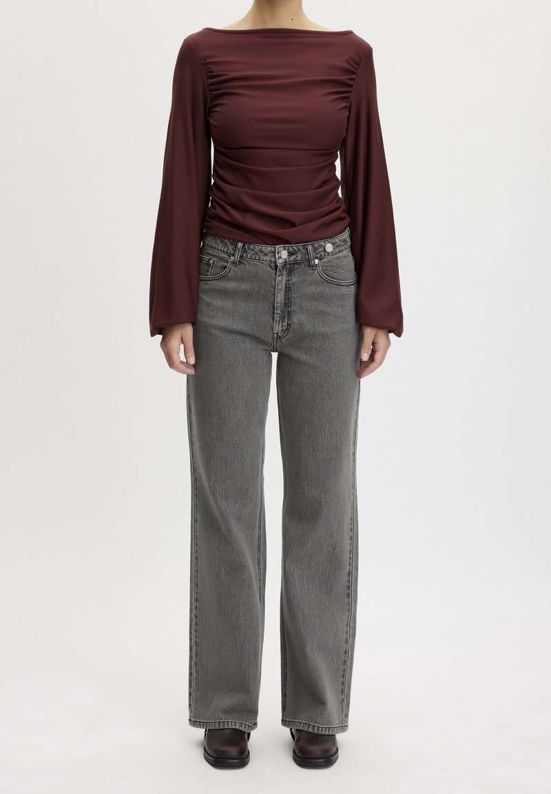 Maglietta a maniche lunghe bordeaux con dettagli arricciati, abbinata a jeans grigi a vita alta. Entrambi i capi presentano una vestibilità comoda e una texture morbida.