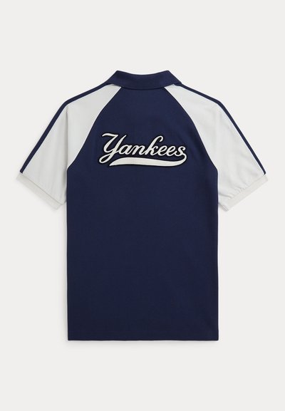 Tumši zilas un baltas īsām piedurknēm polo krekls ar uzšūtu uzrakstu "Yankees" aizmugurē kursīvā fontā.