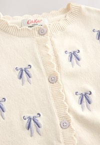 Cream cardigan with light purple ribbon embroidery, ribbed neckline, scalloped trim, and purple buttons down the front. Soft knit material.