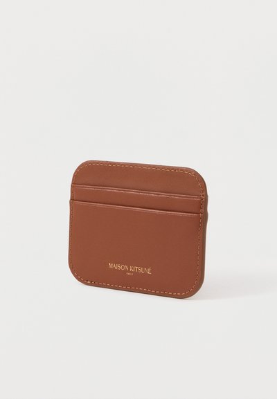 Καφέ δερμάτινη θήκη καρτών με τέσσερις θήκες για κάρτες, λεία υφή και ανάγλυφο λογότυπο σε χρυσό. Ορατές στρογγυλεμένες άκρες και αντίθεση ραφής.