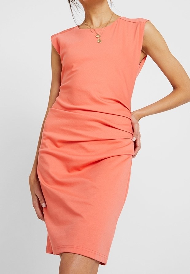 Orange ärmlös klänning i stretchigt tyg, figurnära siluett med rynkdetalj vid midjan, slät textur, knälång nederdel.