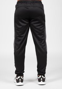 Zwarte sportbroek met een slim fit, elastische tailleband en reflecterende zijaccenten, gecombineerd met zwart-witte sportschoenen.