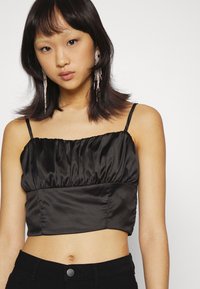 Top cropped de satin preto com busto franzido, alças finas ajustáveis e textura suave. Usado com calças pretas de cintura alta.