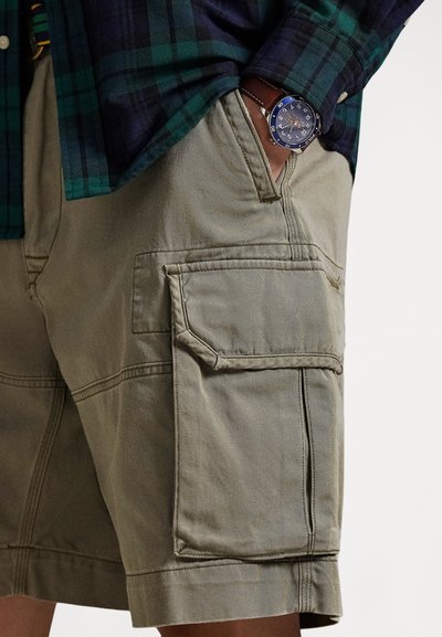 Béžové cargo šortky z pevné látky, s bočními kapsami, prošitými detaily a volným střihem. Nošeny s károvanou košilí.