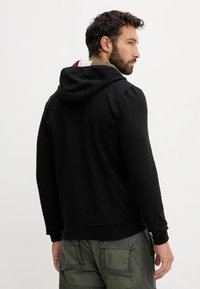 Felpa nera con cappuccio realizzata in un tessuto morbido, con orlo e polsini a coste, e rivestimento interno a contrasto visibile nel cappuccio.