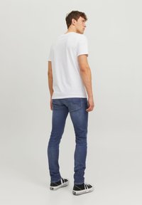 T-shirt blanc à manches courtes, jeans ajustés bleu et baskets noires avec semelles blanches. Tissu lisse et design classique. Look minimaliste.