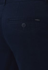 Ciemnoniebieskie spodnie wykonane z teksturowanej tkaniny, z tylną kieszenią zapinaną na guziczek i małą metką marki.