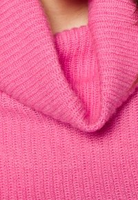 Maglione lavorato a maglia di un rosa acceso, caratterizzato da un ampio collo pieghevole. La texture è a coste, con un aspetto morbido e caldo.
