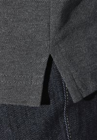 Graues Kurzarmhemd aus strukturierter Baumwolle, mit seitlichen Schlitzen und genähten Nähten, kombiniert mit dunklen Jeans.