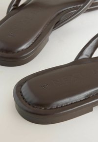 Gros plan sur des sandales en cuir marron foncé avec une zone de l’orteil carrée matelassée et des coutures visibles sur fond blanc.