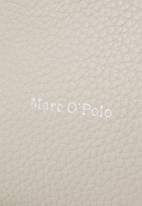 Bežová textúrovaná koža so vzorom embosovaného loga "Mare O'Polo" v bielej farbe. Povrch zobrazuje jemný vzor zrna.