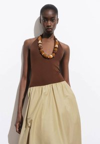 Hnědý halter top s béžovou sukní, doplněný masivním náhrdelníkem z vícebarevných korálků. Hladká tkanina s nařaseným pasem.