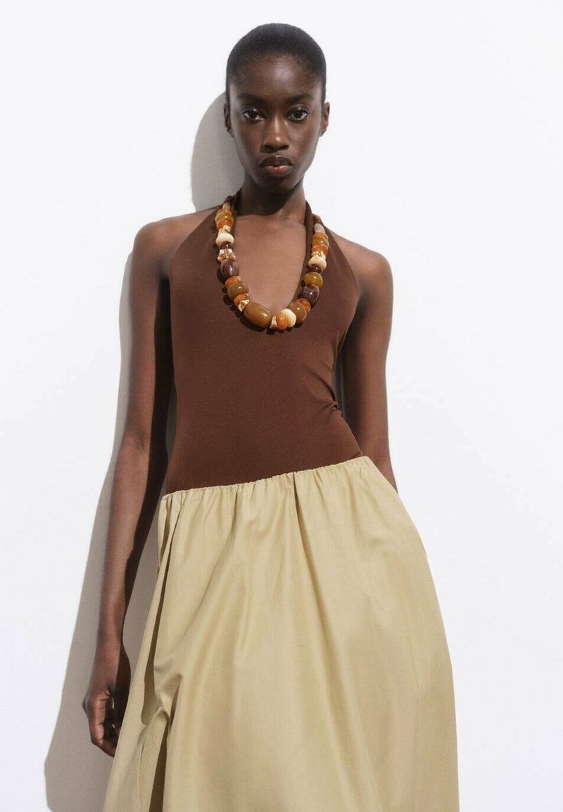 Hnědý halter top s béžovou sukní, doplněný masivním náhrdelníkem z vícebarevných korálků. Hladká tkanina s nařaseným pasem.