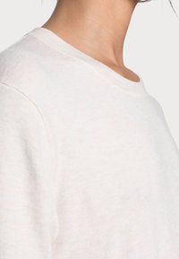 Sweatshirt beige clair à col rond, doté d'un tissu doux et texturé et d'une coupe décontractée, présentant des détails de couture minimalistes.
