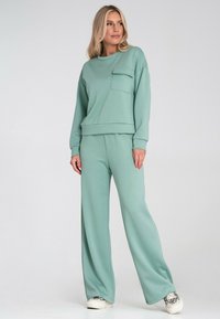 Jasnozielony krótki sweter z kieszenią i pasującymi szerokimi spodniami, wykonany z miękkiego materiału, o luźnym kroju i ściągaczach.