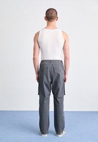 Gray cargo pants with elastic waistband and multiple pockets, paired with a white tank top, viewed from the back on a light blue surface.