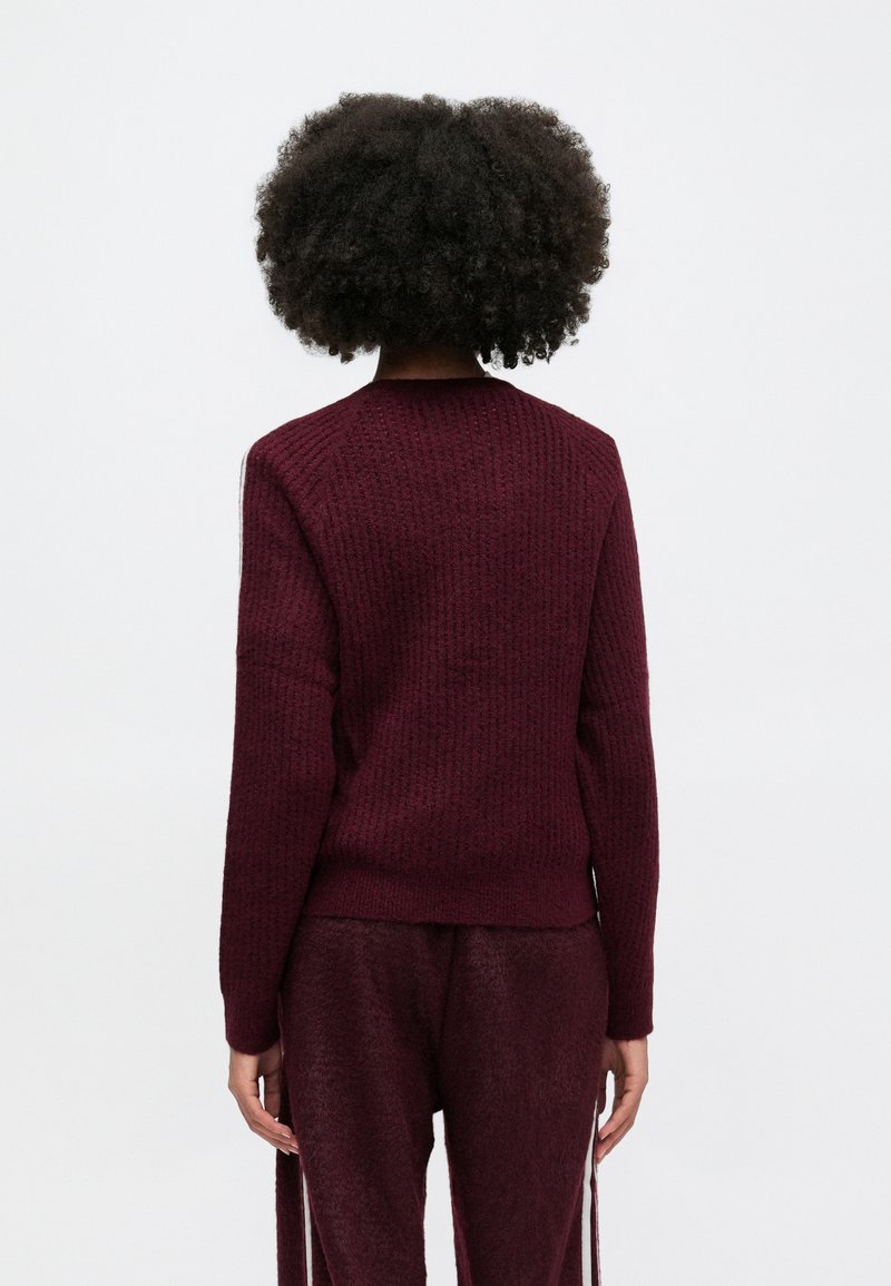 Burgunderfarbener Strickpullover mit gerippter Textur, Rundhalsausschnitt und langen Ärmeln, der einen leicht verkürzten Saum hinten aufweist.