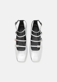 Ballet flats métalliques argentés avec des orteils carrés, plusieurs fines lanières et boucles. La doublure intérieure est noire avec une texture lisse.