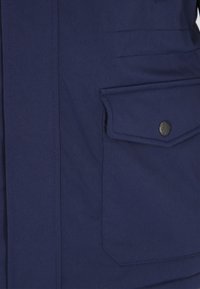 Tengerészkék dzseki sima textúrával, nagy elülső zsebbel, patentos záródással és tiszta varrásokkal a varratok mentén.