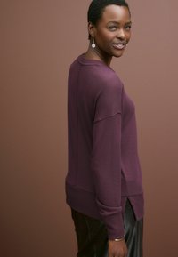 Maglione leggero di un profondo viola con orlo a costine, aperture laterali e spalle scese. Abbinato a pantaloni in pelle scura e sofisticata.