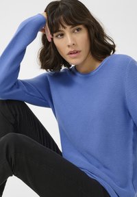 Blau gerippter Langarmpullover mit runder Halslinie, kombiniert mit schwarzen strukturierten Hosen. Lässiger Look mit weichem Stoff und lockerer Passform.