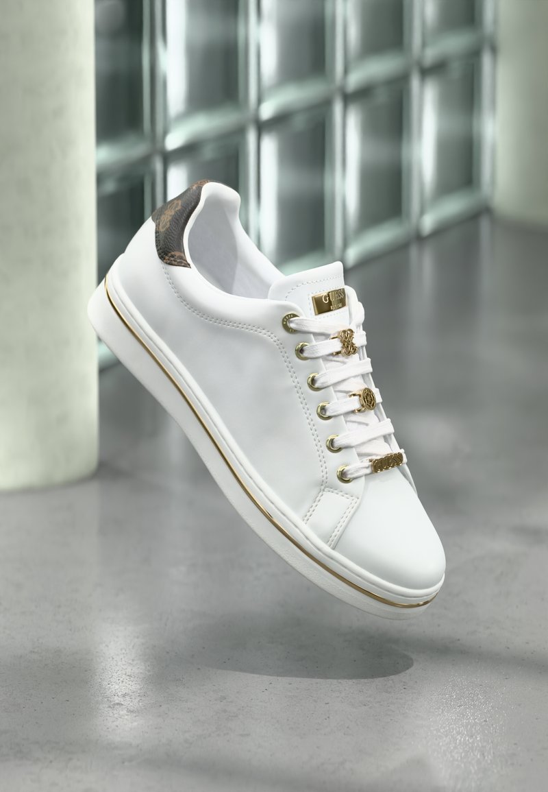 Valged sneakerid kuldsete silmadega, tekstureeritud pruuni rõhuasetusega kandadel ja siledal viimistlusel. Omab ümarat varvata ja tikitud detaile.