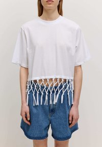 Witte cropped t-shirt met een geknotte franjes detail aan de onderrand. Gekenmerkt door denim shorts. Korte mouwen en een ronde halslijn.