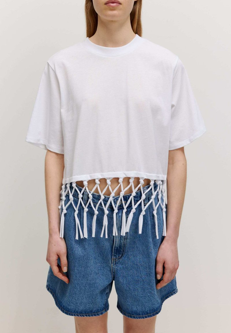 Witte cropped t-shirt met een geknotte franjes detail aan de onderrand. Gekenmerkt door denim shorts. Korte mouwen en een ronde halslijn.