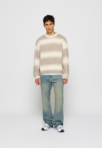 Beige and cream striped knit sweatshirt with a round neckline and ribbed cuffs, paired with light blue jeans and black and white sneakers.