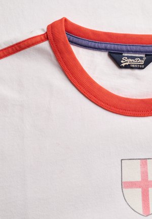 Weißes T-Shirt mit rotem Kragen und Ärmelsaum, SuperDry-Label und teilweisem roten Kreuzschild-Emblem auf der Brust.