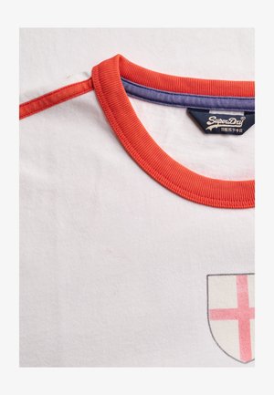 Weißes T-Shirt mit rotem Kragen und Ärmelsaum, SuperDry-Label und teilweisem roten Kreuzschild-Emblem auf der Brust.
