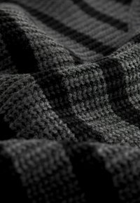 Tissu tricoté gris foncé avec un motif texturé, présentant un aspect tissé et de douces ondulations, mettant en valeur son apparence douce et confortable.