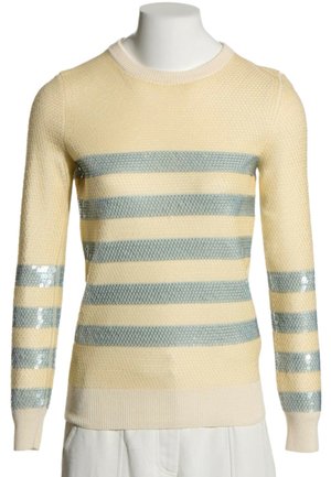 Suéter de punto crema con tela texturizada y franjas horizontales plateadas brillantes en el pecho y las mangas, expuesto en un maniquí blanco.