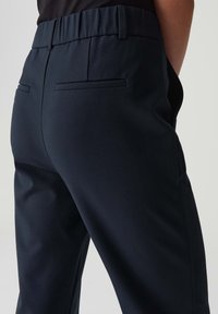 Marineblauwe op maat gemaakte broeken met een soepele textuur, elastische tailleband en twee achterzakken met minimale stikdetails.