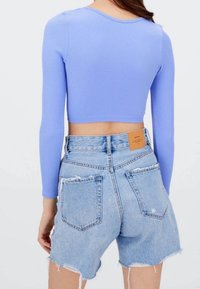 Jasnofioletowy prążkowany krótki top z długim rękawem, zestawiony z przetartymi, jasnoniebieskimi, wysokim stanem szortami dżinsowymi, z brązową metką na pasku.