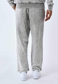 Pantalones de chándal gris claro con una textura suave, corte relajado y banda elástica acanalada en la cintura. Cuenta con bolsillos laterales y puños ajustados en los tobillos.