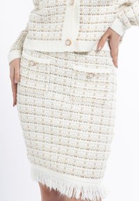 Woven sukýnka v krémové barvě se zlatými akcenty, s texturovaným kostkovaným vzorem, dvěma kapsami se zdobnými knoflíky a střapcovým lemem.