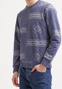 Felpa a maniche lunghe blu navy con motivi geometrici grigio chiaro, dotata di colletto rotondo e polsini a costine. Vestibilità casual, tessuto testurizzato.