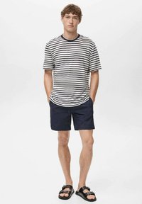 T-shirt à manches courtes rayé en crème et marine, associé à un short marine. Le modèle porte des sandales noires. Tenue d'été simple et décontractée.