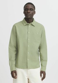 Green long-sleeve button-up shirt with a chest pocket, made of lightweight fabric, featuring a collared neck and white buttons.