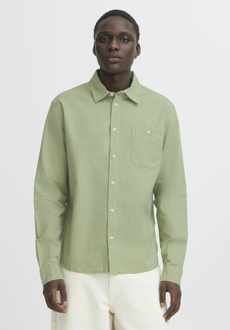 Green long-sleeve button-up shirt with a chest pocket, made of lightweight fabric, featuring a collared neck and white buttons.