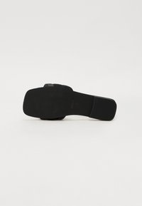 Black high-heeled shoe viewed from the bottom; smooth sole, square toe, minimal detailing, and a flat heel provide a modern design.