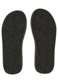 Semelles de chaussures en caoutchouc noir avec un motif texturé comportant des formes géométriques et des logos, conçues pour l'adhérence et la traction.